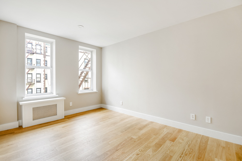 A room with wooden floors and a window showing a building outside.